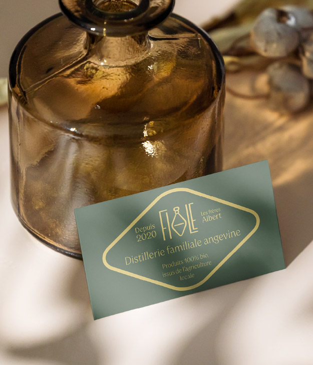 Le logo Fiole mis en scène sur une table avec un flacon en verre marron. Le logo est en forme de losange aux bords arrondis