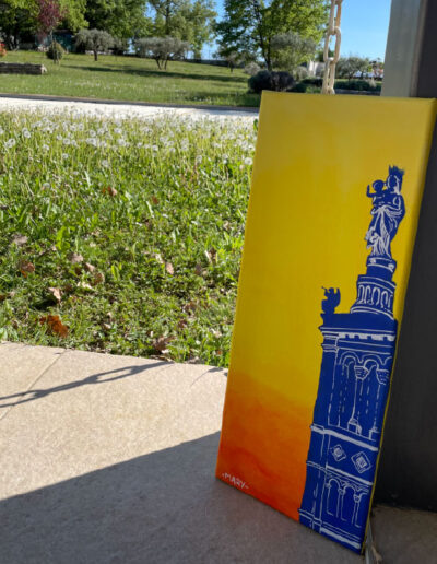 Un tableau représentant la statue de la vierge de Notre dame de la garde, bleue sur fond aux couleurs du coucher de soleil
